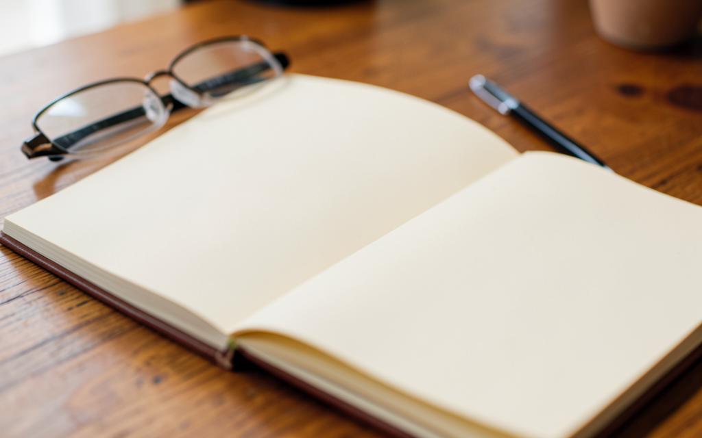 An open printed feature article on a wooden table beside reading glasses